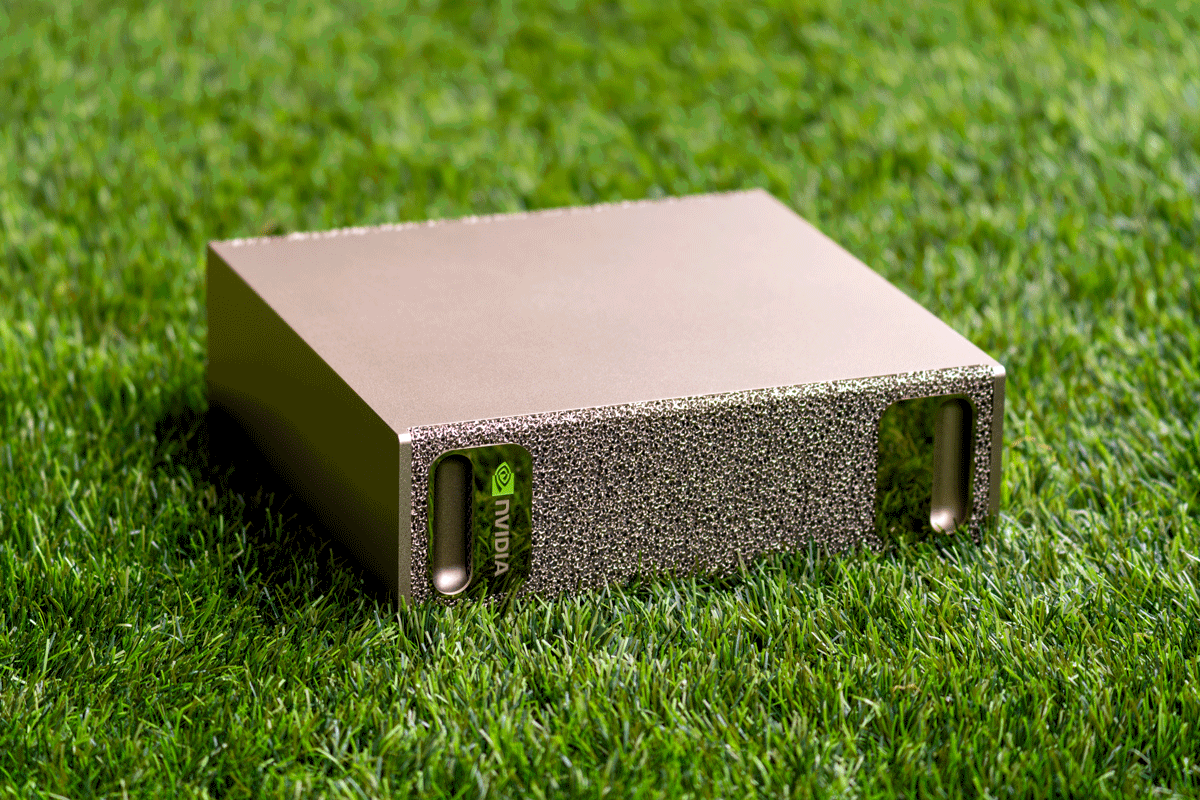 An NVIDIA DGX Spark, a small metallic box with a perforated front panel, standing on green grass.